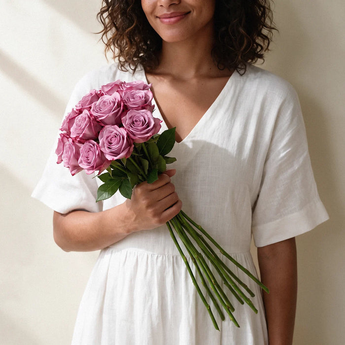Small size: 12 mauve-pink roses on long stems held in one hand by a smiling woman with curly hair, Fabulous Flowers South Africa