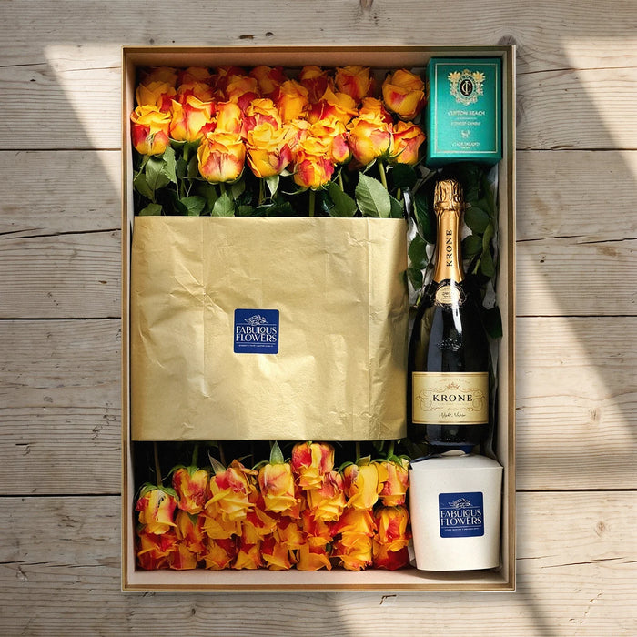 Striking Opulence Gift Box from above on a pine table: 40 orange roses, Krone Night Nectar, a Cape Island Clifton Beach candle and a boxed cupcake, Fabulous Flowers South Africa