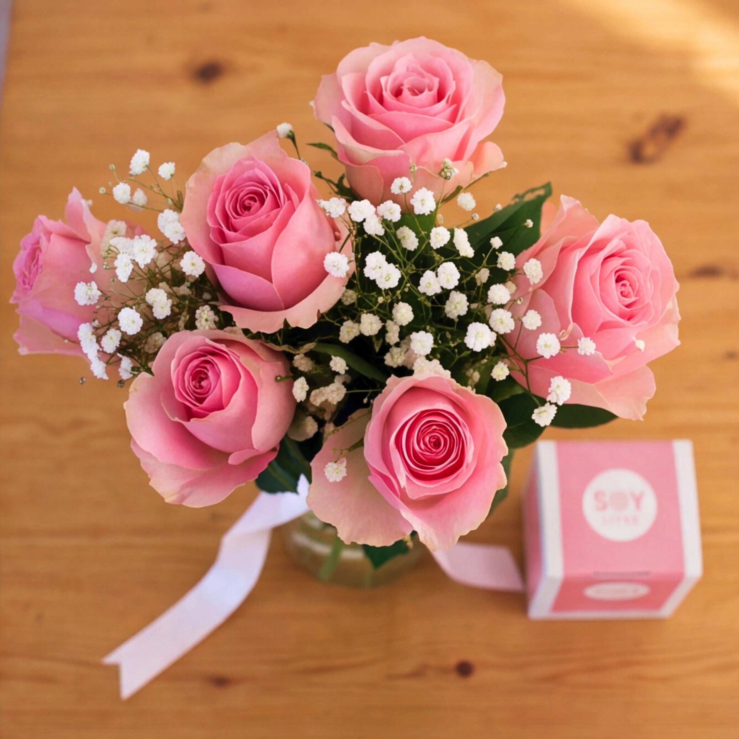Overhead view of A Rosy Glow pink rose arrangement and Soy Lites candle