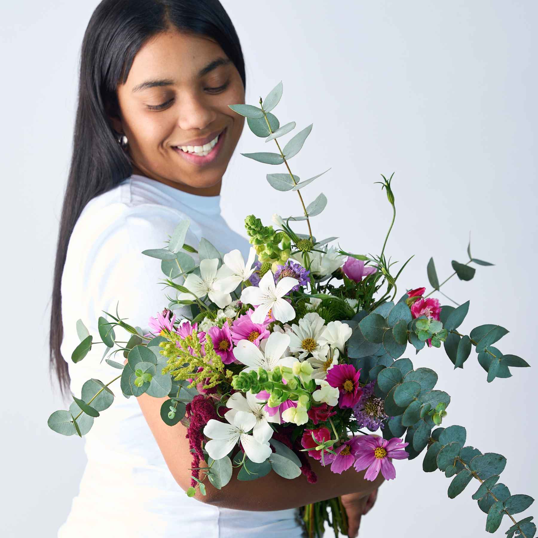 A woman smiling while holding a large bouquet of wildflowers and greenery, representing the 'A Walk in the Woods' flower bouquet.