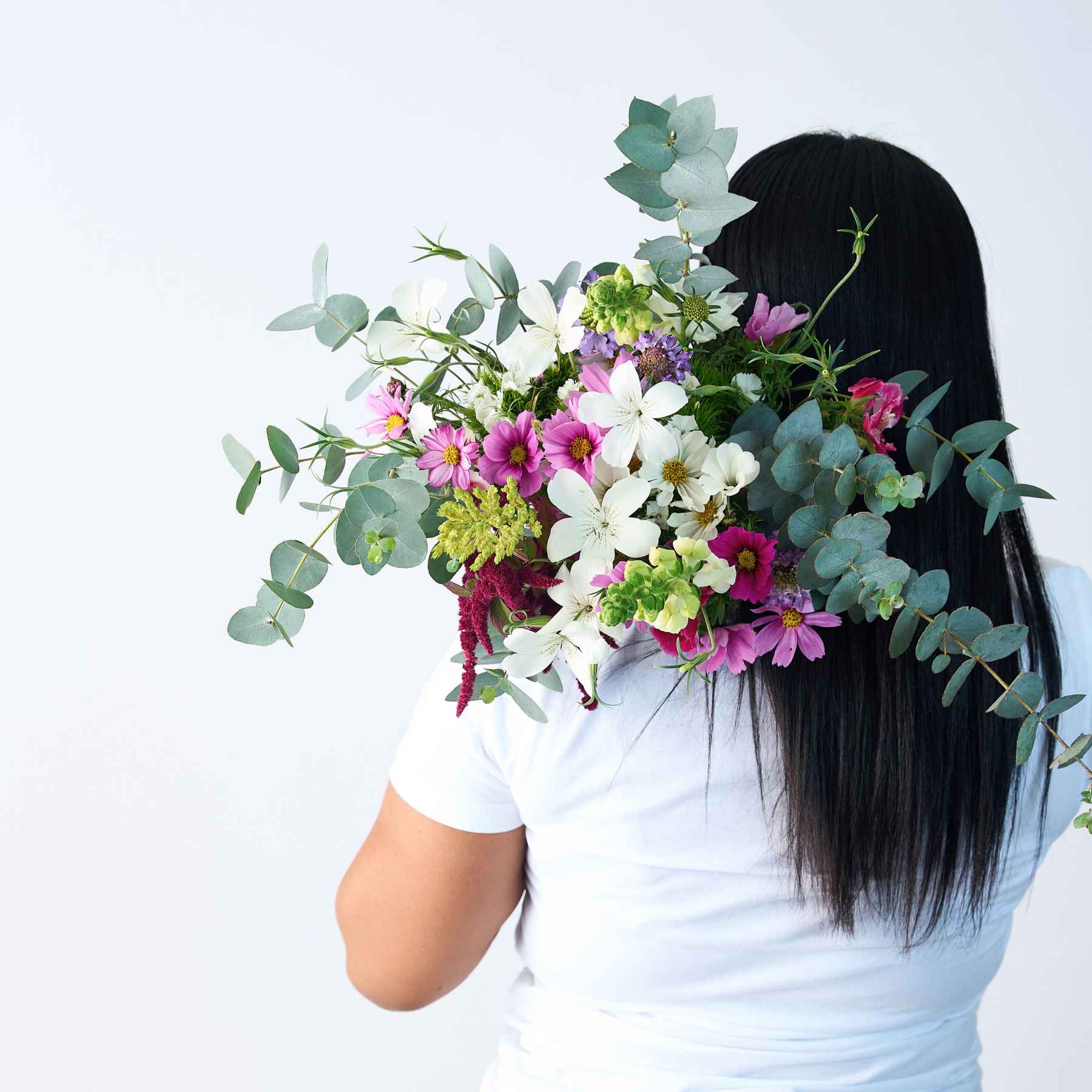 Back view of a woman holding a lush bouquet of wildflowers and greenery over her shoulder, symbolising the natural beauty of the 'A Walk in the Woods' bouquet.