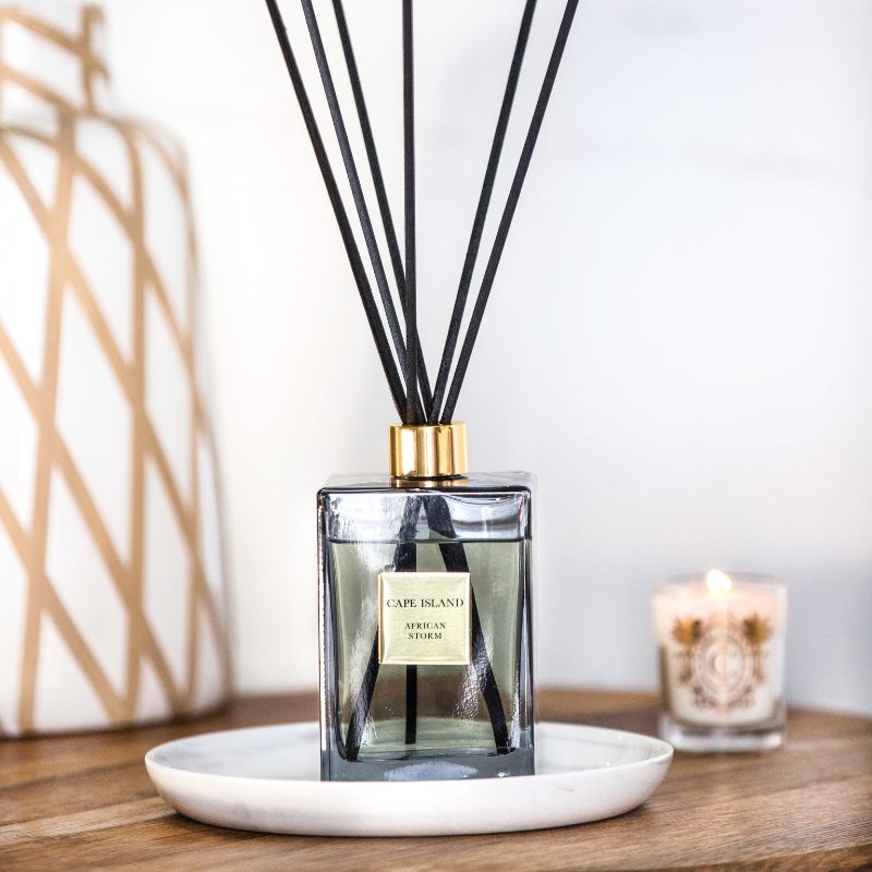 Reed diffuser with black sticks on a white plate, candle in the background