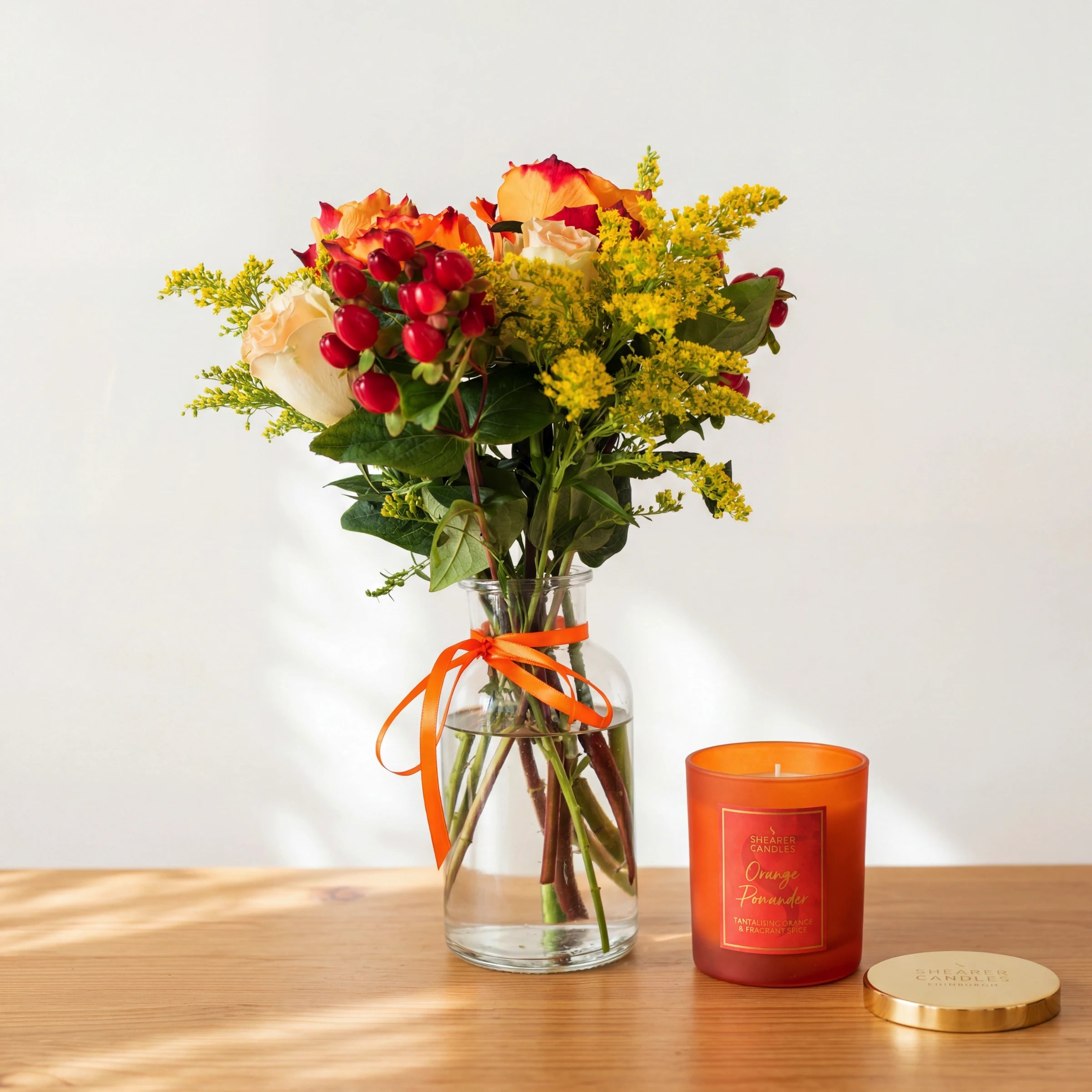 Amber & Spice candle gift set: an autumn rose posy in a glass vase beside the Shearer Candles Orange Pomander candle