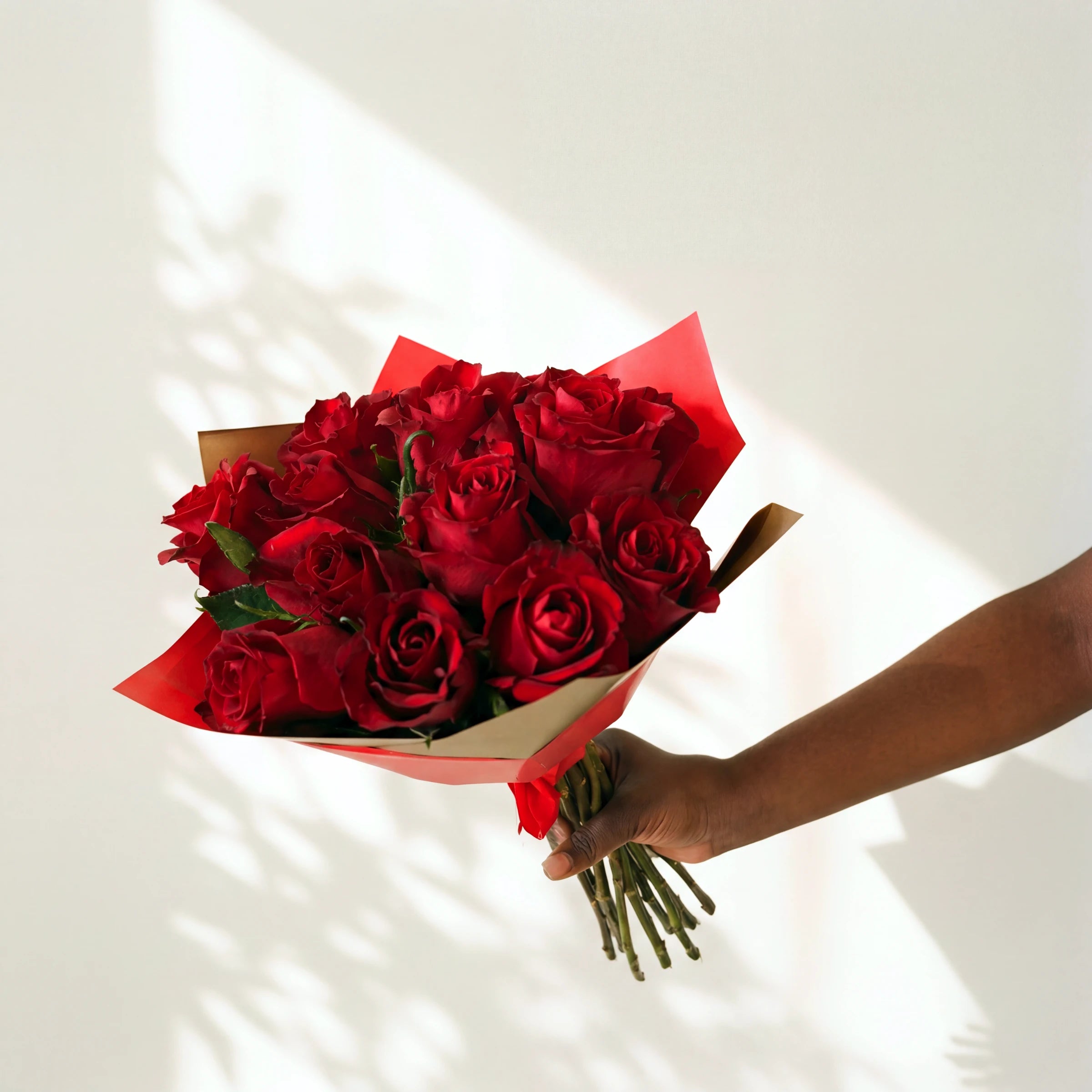 A dozen red roses hand-tied in red and gold wrap, held out by a florist from the Amour bouquet range