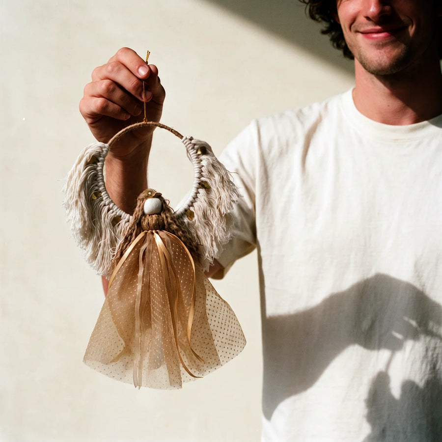 Smiling man in a white t-shirt holding out a handmade gold Christmas angel by its gold hanging thread, Fabulous Flowers South Africa