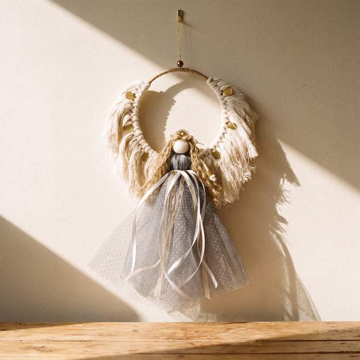 Handmade macramé Christmas angel with cream wings, gold leaves and a dove-grey tulle skirt hanging on a sunlit cream wall, Fabulous Flowers South Africa