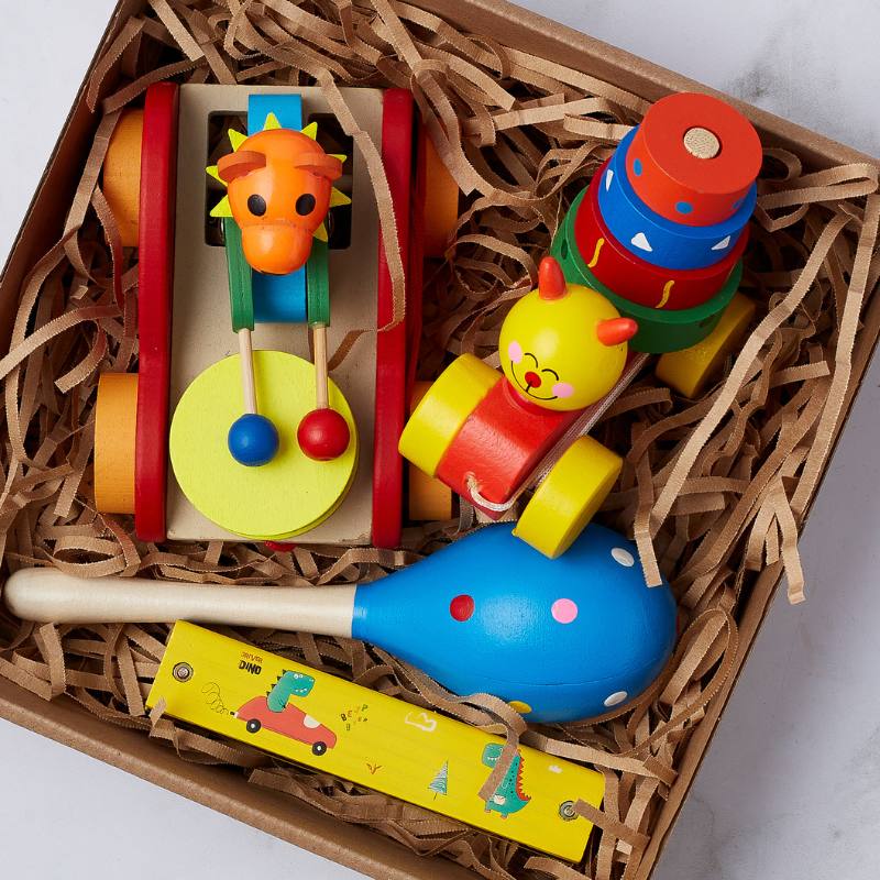 Close-up of Baby's First Toy Set with wooden stacking rings, a lion toy, maraca, and a dinosaur rattle, perfect for a baby's first playtime.