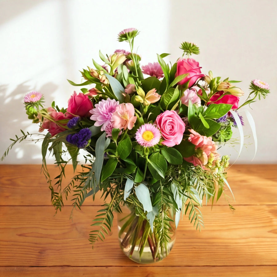 The Beauty in a Bottle pink and purple garden arrangement in a glass jar on a wooden table
