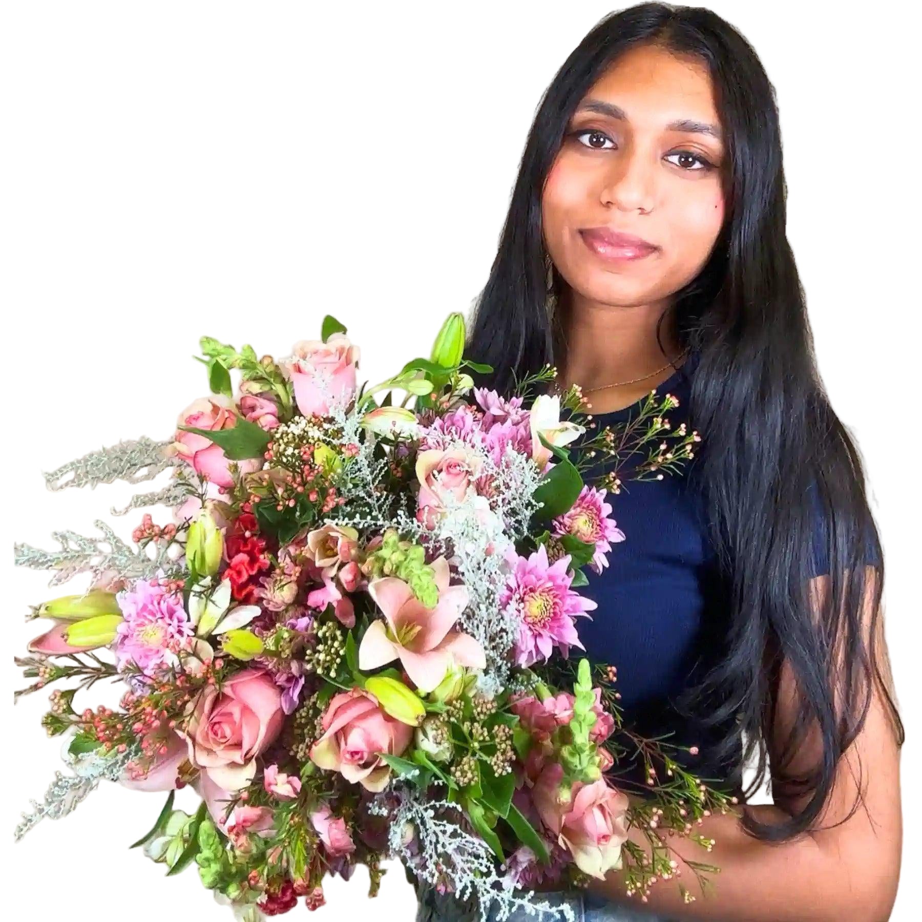A smiling woman holding a stunning bouquet of mixed pink and white flowers, featuring roses, lilies, and assorted greenery. Bella’s Flower Bouquet. Fabulous Flowers and Gifts.