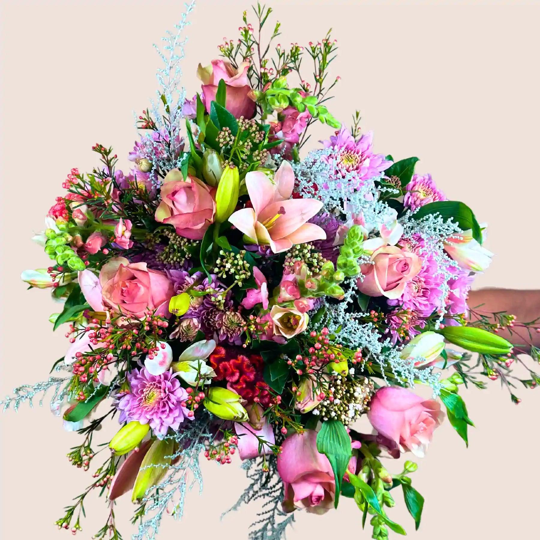 A smiling woman holding a stunning bouquet of mixed pink and white flowers, featuring roses, lilies, and assorted greenery. Bella’s Flower Bouquet. Fabulous Flowers and Gifts.