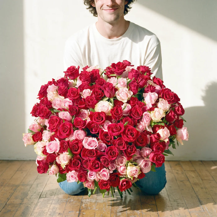 Smiling man kneeling on a wooden floor holding out a giant bouquet of 300 red and blush pink roses, Fabulous Flowers South Africa