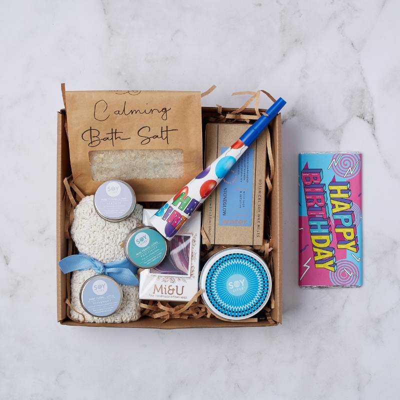 Birthday Treats & Tranquility Gift Box with calming bath salts, soy candles, a birthday chocolate, a party blower, and artisanal soap.