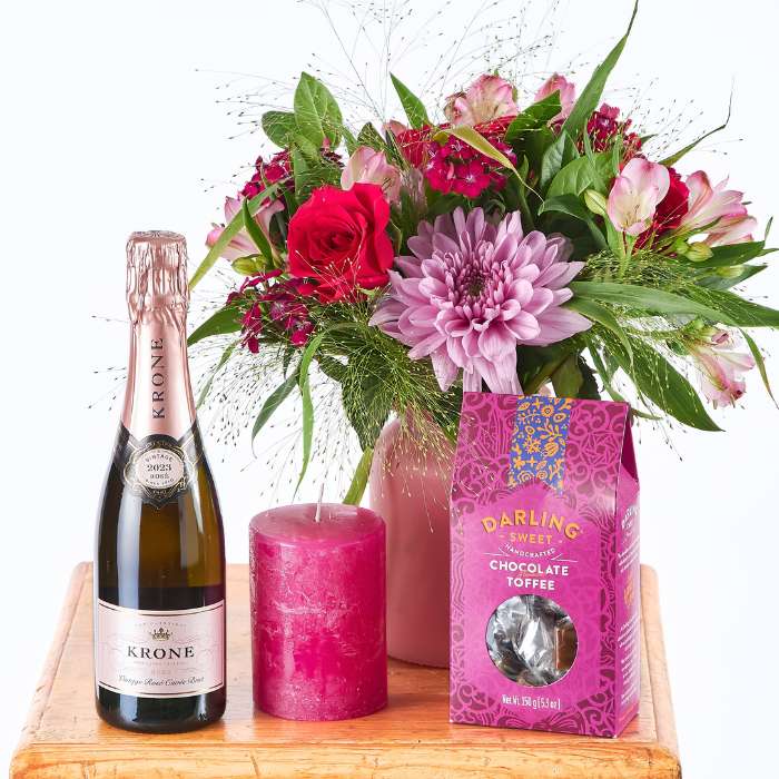 Luxurious gift arrangement featuring a floral bouquet, pink candle, champagne, and artisan chocolate.