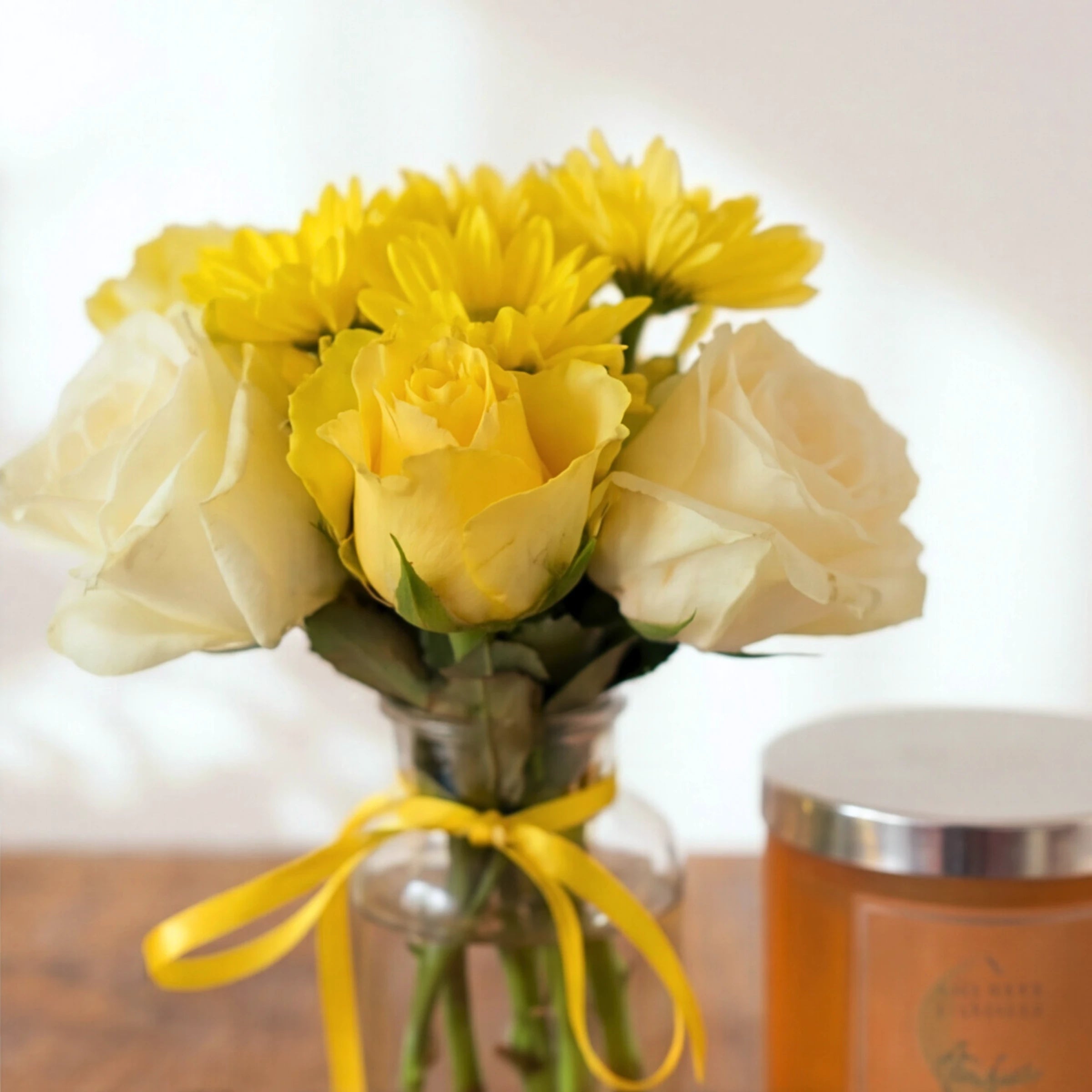 Close-up of the yellow and cream rose posy in the Bloom & Glow gift set, with the candle behind