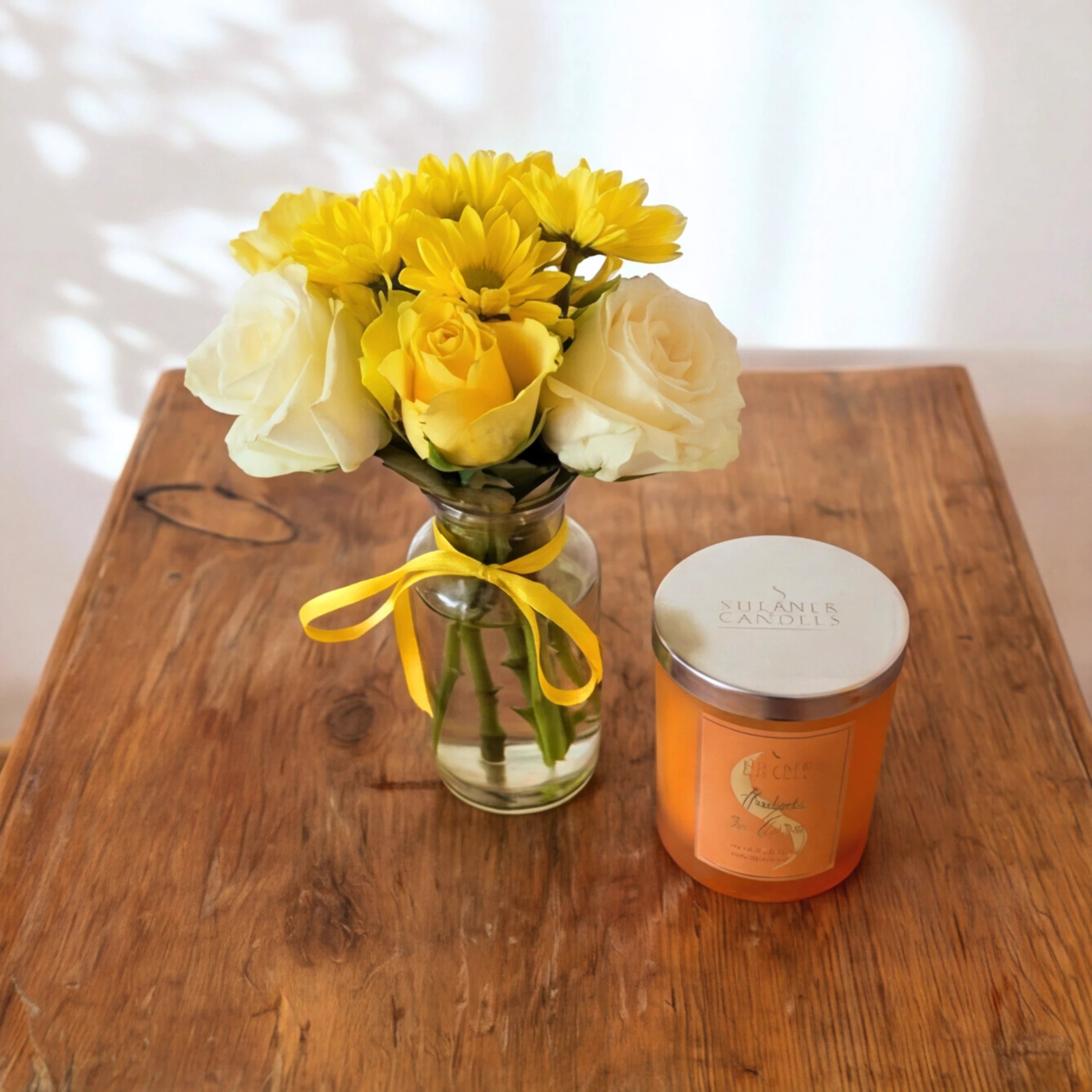 Bloom & Glow gift set, a sunny rose posy beside the Shearer Amber & Rose candle on a wooden table