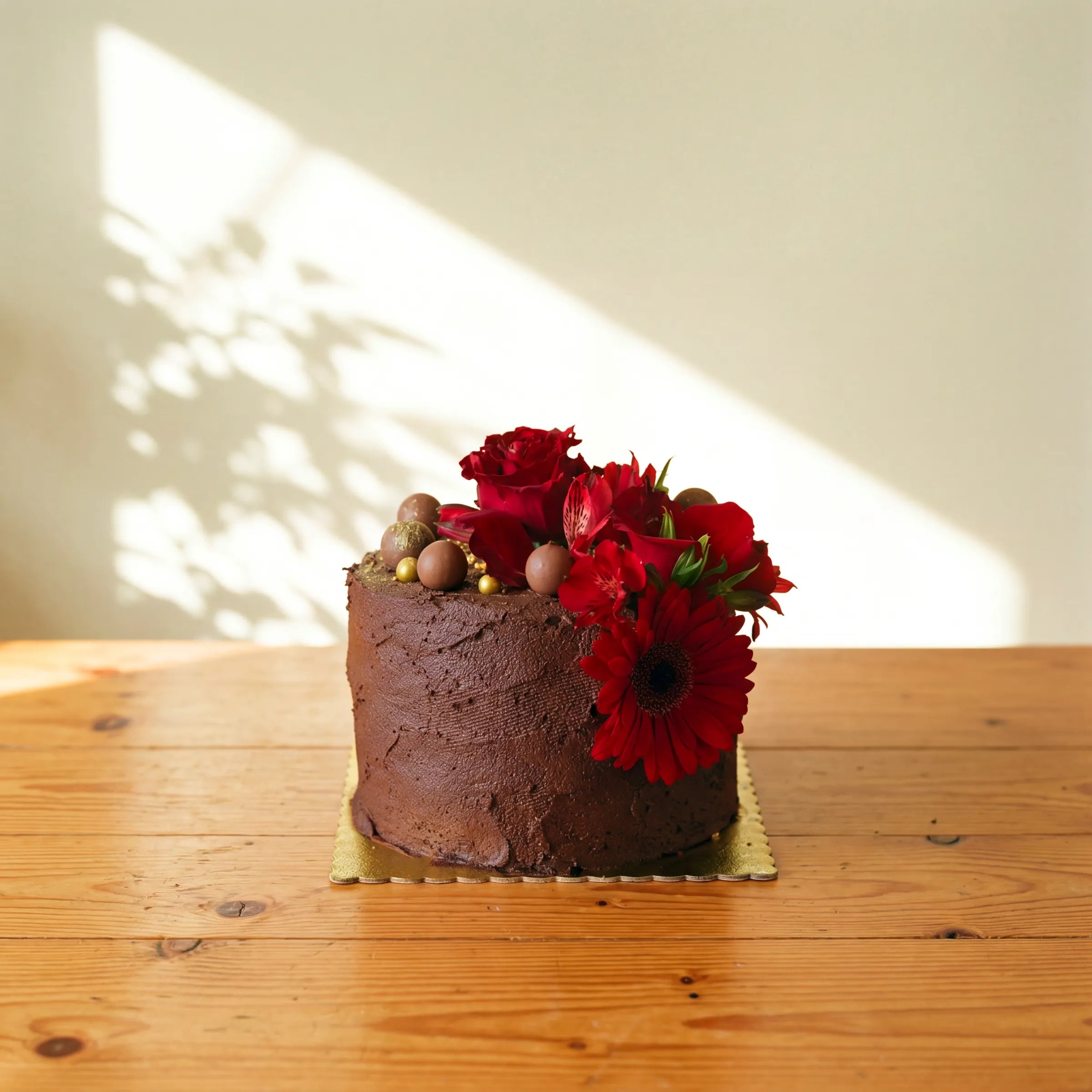 Single tier chocolate cake with rich ganache frosting, topped with fresh red roses, red gerbera daisies, red alstroemerias and chocolate truffles, hand-finished by Fabulous Flowers Cape Town