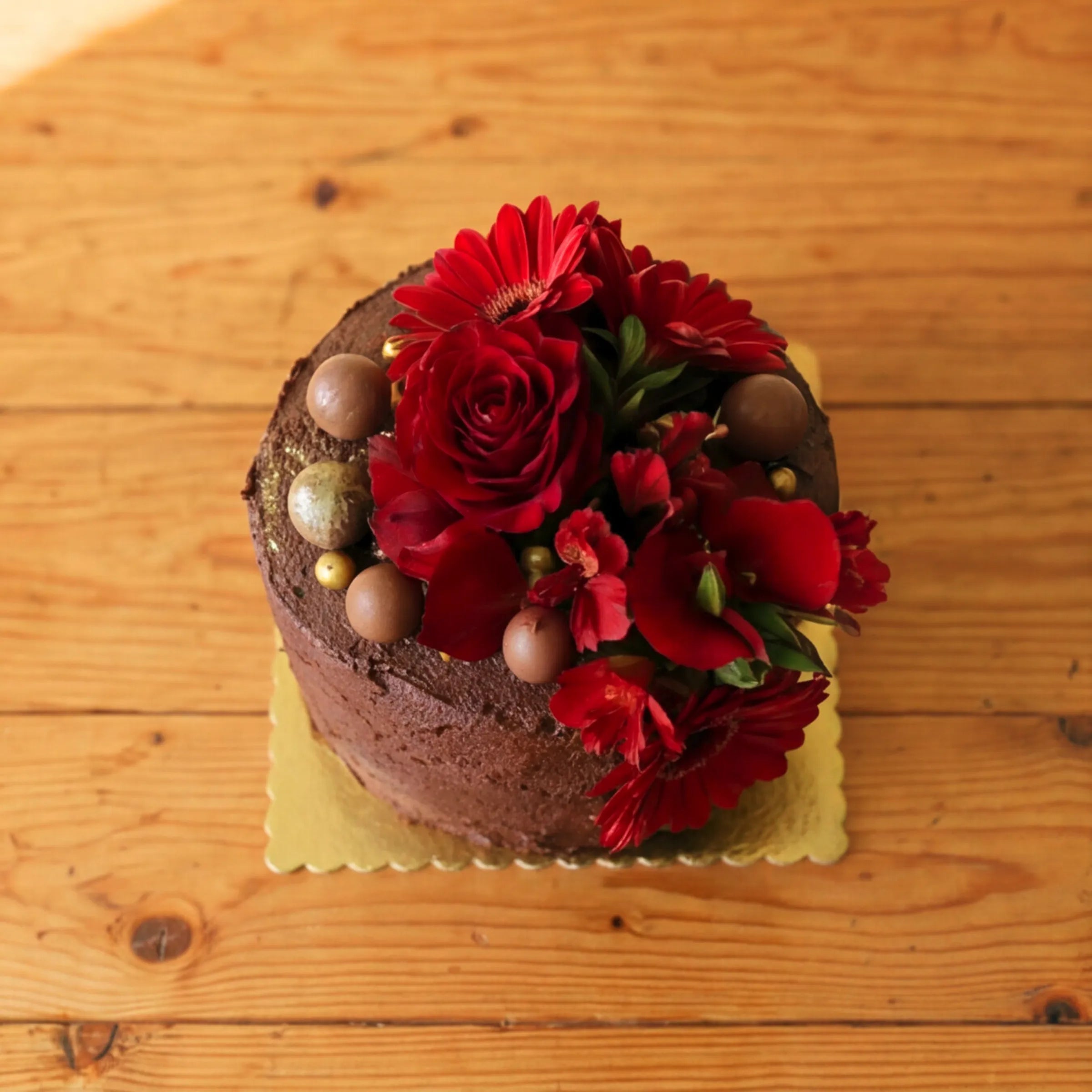 Overhead view of a Fabulous Flowers chocolate celebration cake showing the floral crown of red roses, red gerbera daisies and chocolate truffles with gold edible pearls