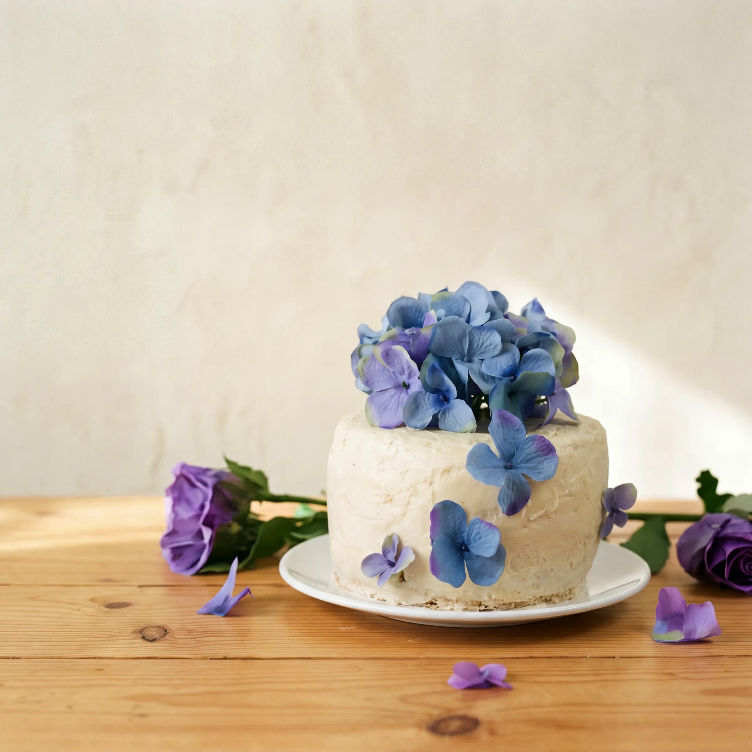 Side angle of Blue Blossom Harmony Madeira Cake showing rustic vanilla icing and blue hydrangea blooms