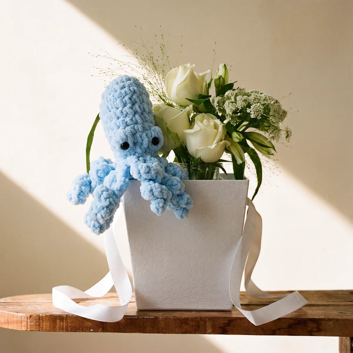 Pale blue crochet octopus sitting on a white flower bag of white roses and Queen Anne's lace on a sunlit pine table, Fabulous Flowers South Africa