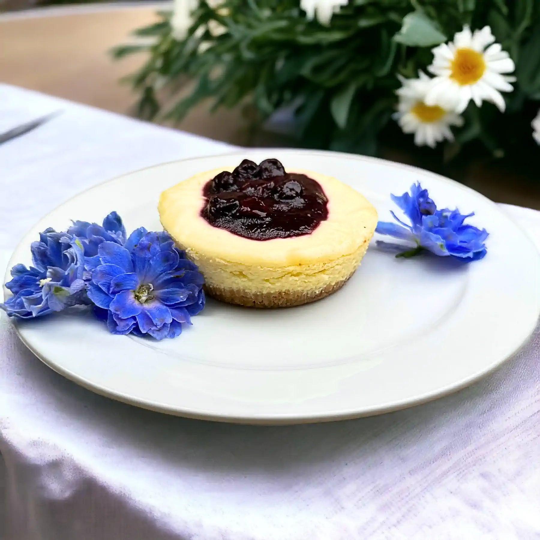 A delectable blueberry cheesecake topped with rich blueberry sauce, adorned with vibrant blue flowers. Fabulous Flowers and Gifts.