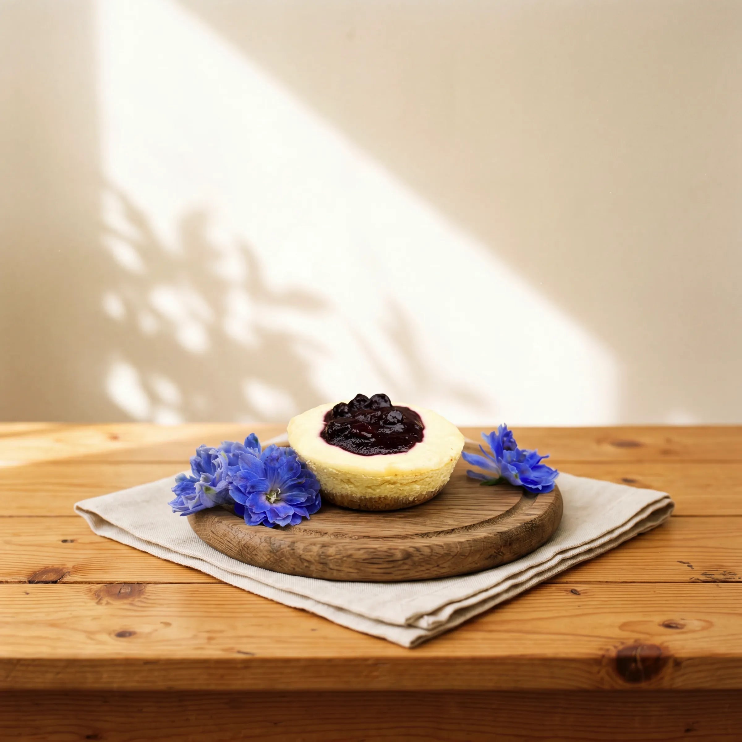 Front view of Blueberry Cheesecake with blueberry compote crown and blue delphinium florals by Fabulous Flowers