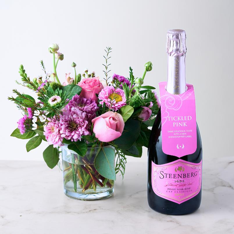 Blush & Bubbles Gift Set featuring a vibrant pink floral arrangement in a glass vase and a bottle of Steenberg Pinot Noir Rosé Cap Classique Brut champagne.