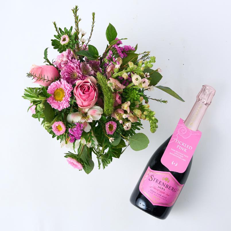 Top view of the Blush & Bubbles Gift Set with a pink floral arrangement and a bottle of Steenberg Pinot Noir Rosé Cap Classique Brut champagne.