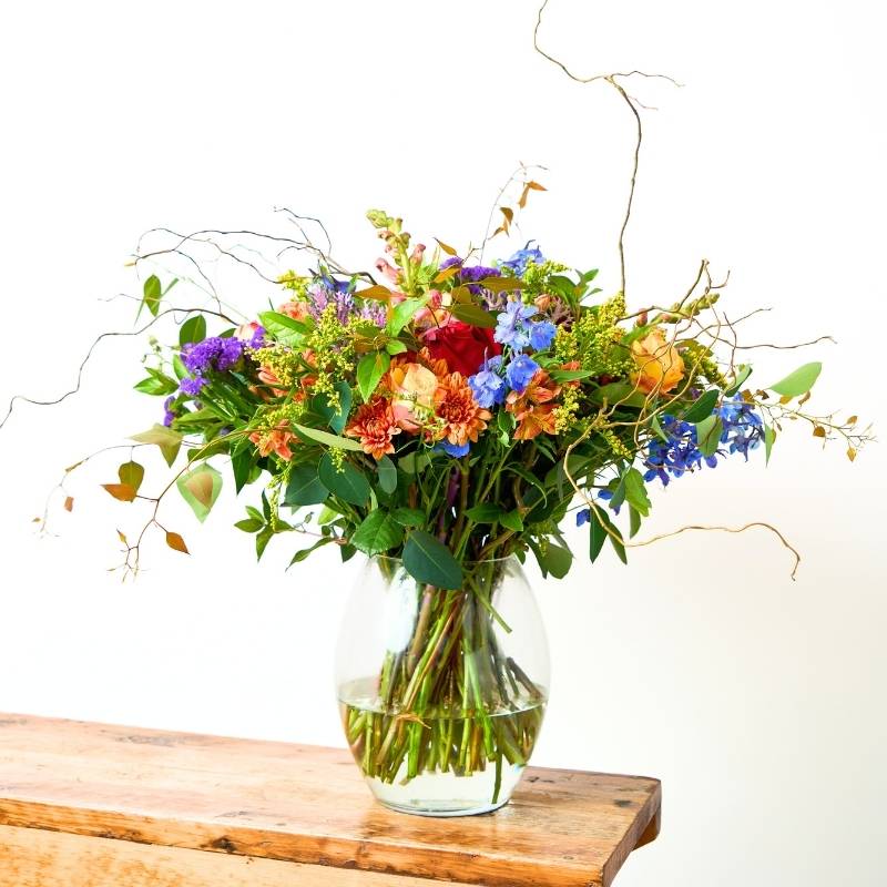Vase arrangement of colouful flowers in a clear vase on a wooden surface with a white background