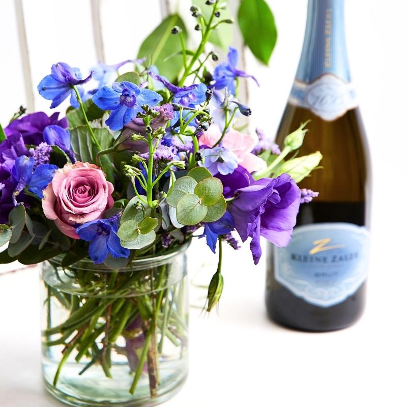 Small blue bouquet with sparkling wine bottle on white background, celebration gift set