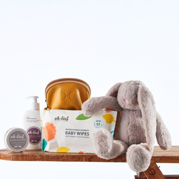 Bunny Love Baby Kit featuring a grey plush bunny, natural baby care products, and biodegradable bamboo baby wipes displayed with a golden monogrammed pouch.