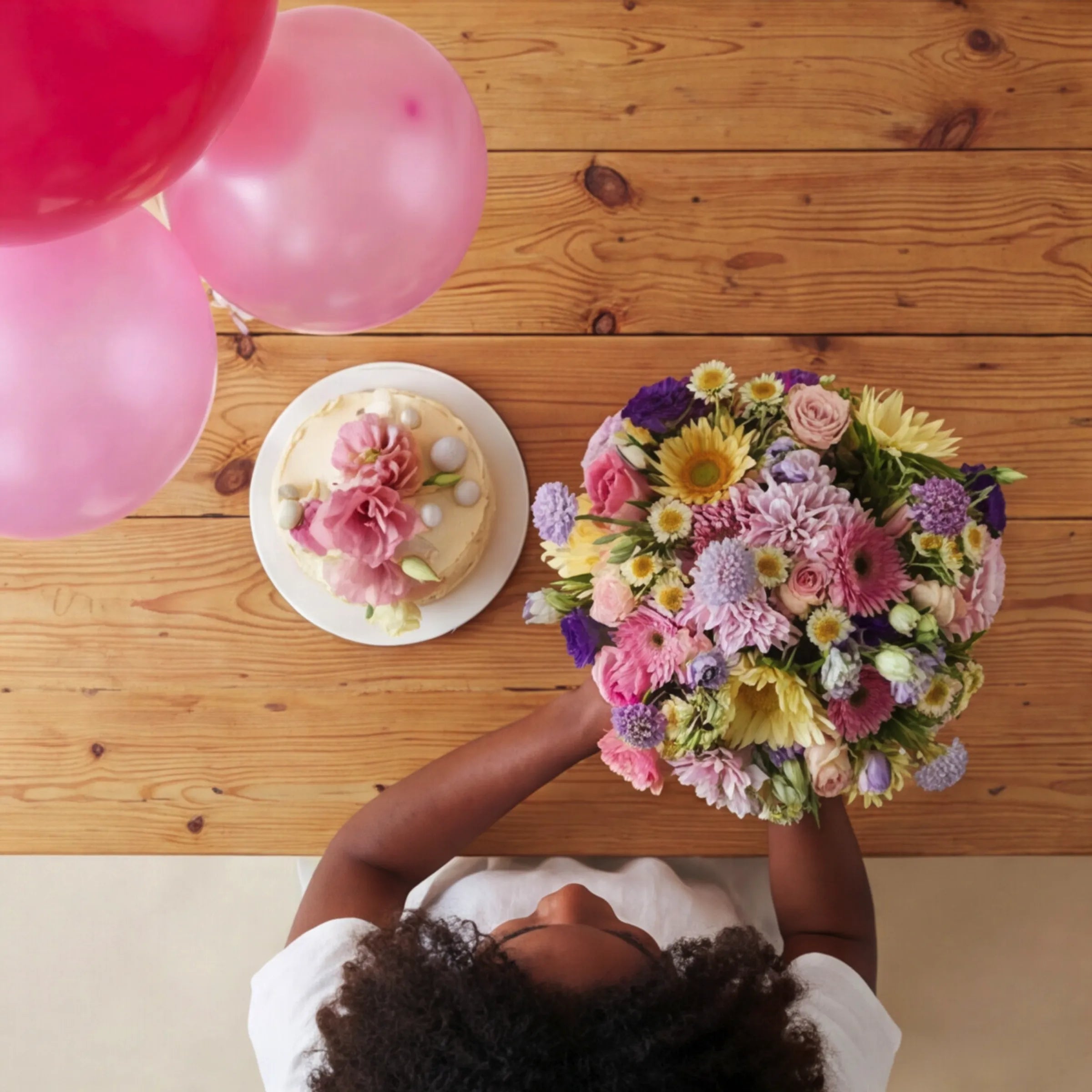 Overhead view of Buttercream Blooms mixed pink, yellow and purple bouquet with balloons and buttercream cake