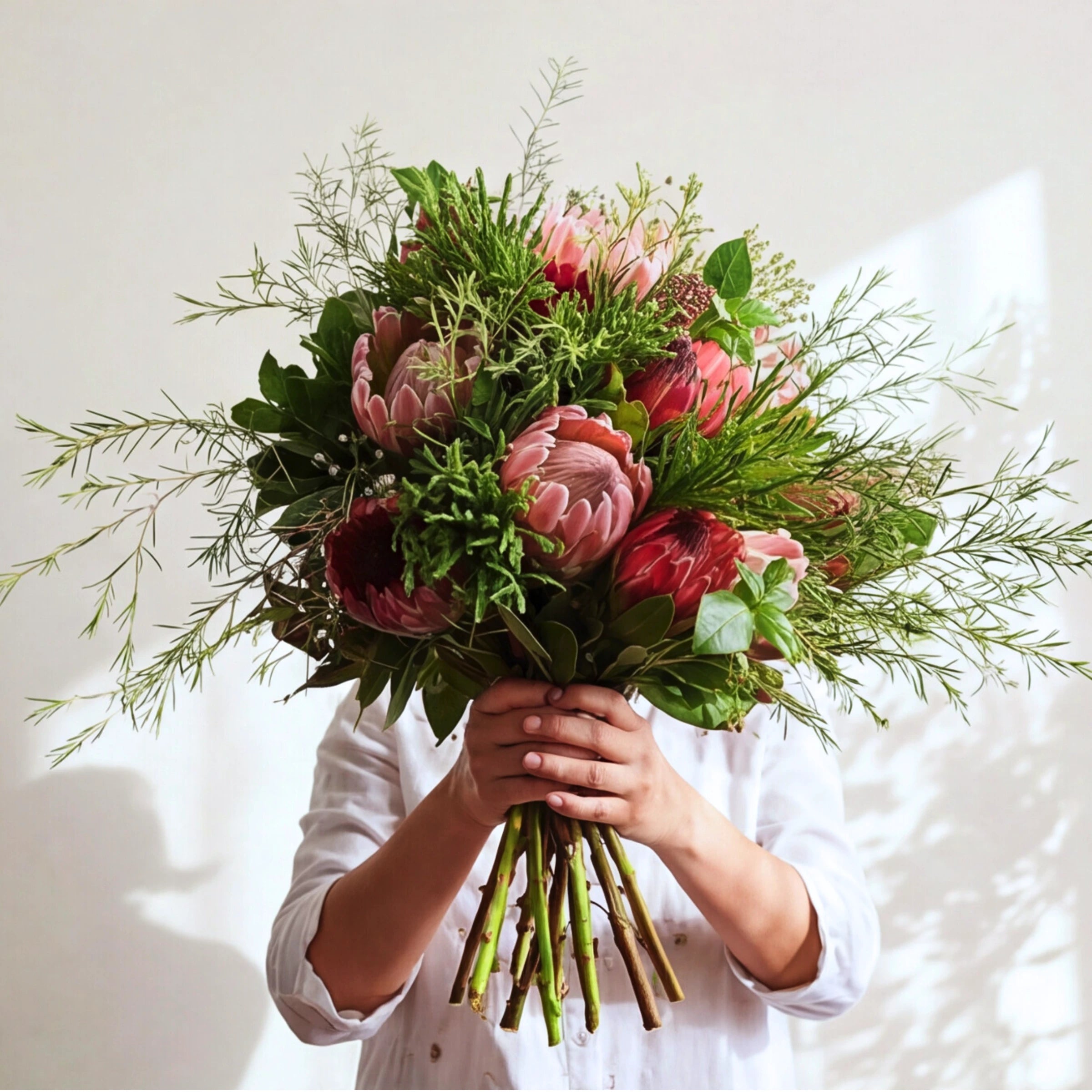 Pink and red proteas with fynbos greenery in the Cape Town Protea Bouquet, stems showing