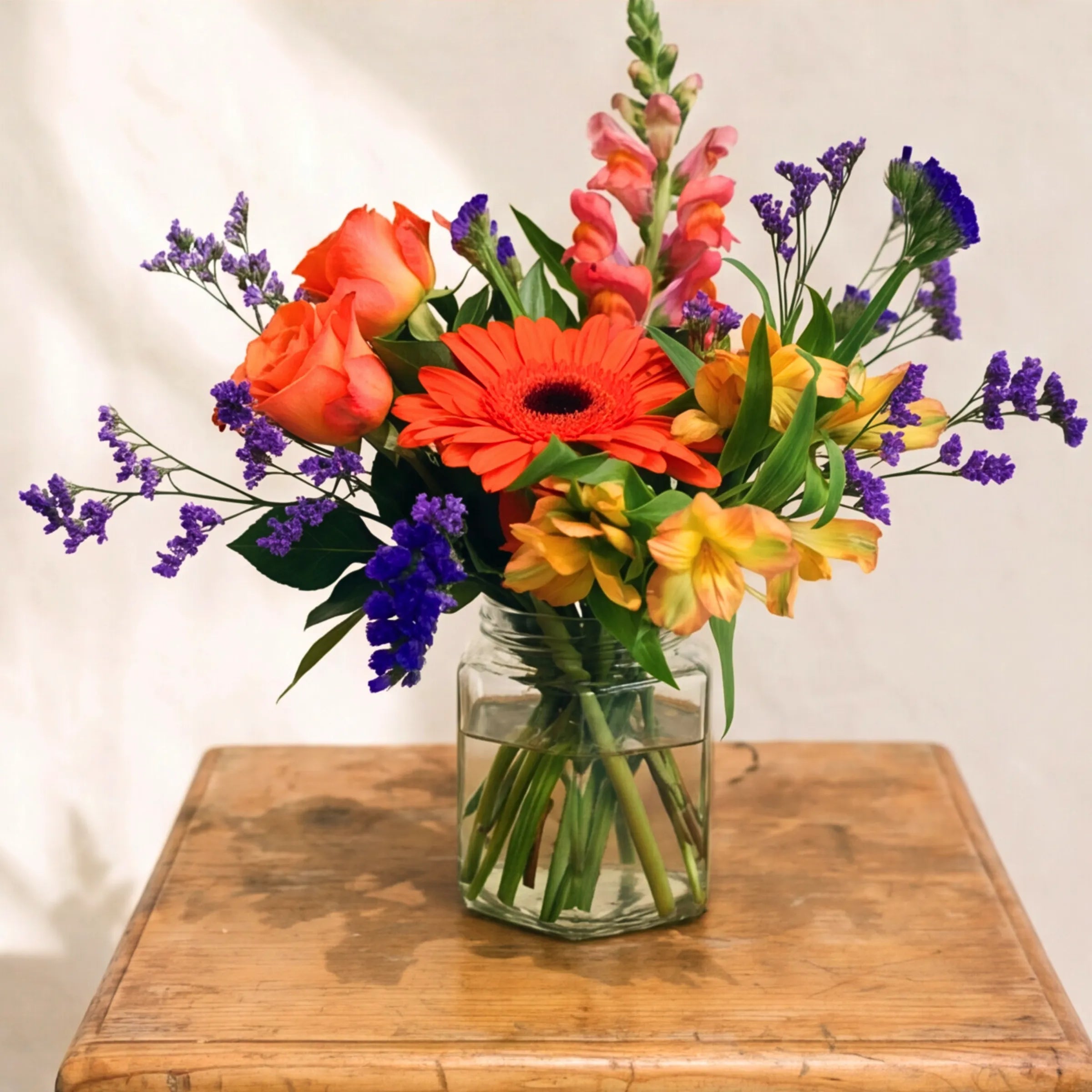 The Carnival in a Jar bouquet from Fabulous Flowers South Africa, an orange gerbera daisy, peach roses, pink snapdragons, yellow alstroemeria and purple statice hand-tied in a small clear glass jar, an affordable multi-coloured flower gift for Cape Town and Johannesburg same-day delivery