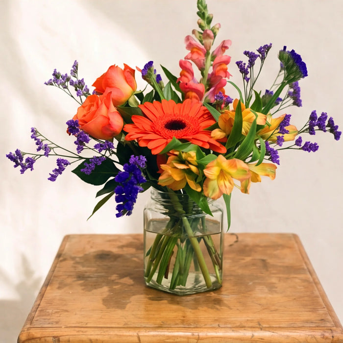 The Carnival in a Jar bouquet from Fabulous Flowers South Africa, an orange gerbera daisy, peach roses, pink snapdragons, yellow alstroemeria and purple statice hand-tied in a small clear glass jar, an affordable multi-coloured flower gift for Cape Town and Johannesburg same-day delivery