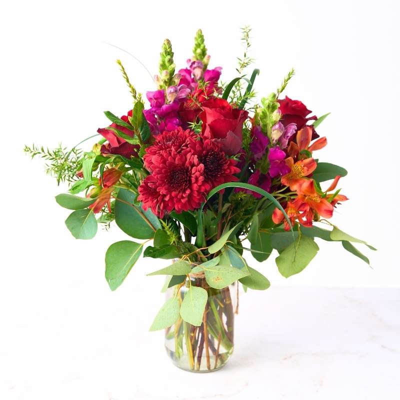 Arrangement of colorful flowers in a clear vase on a white background