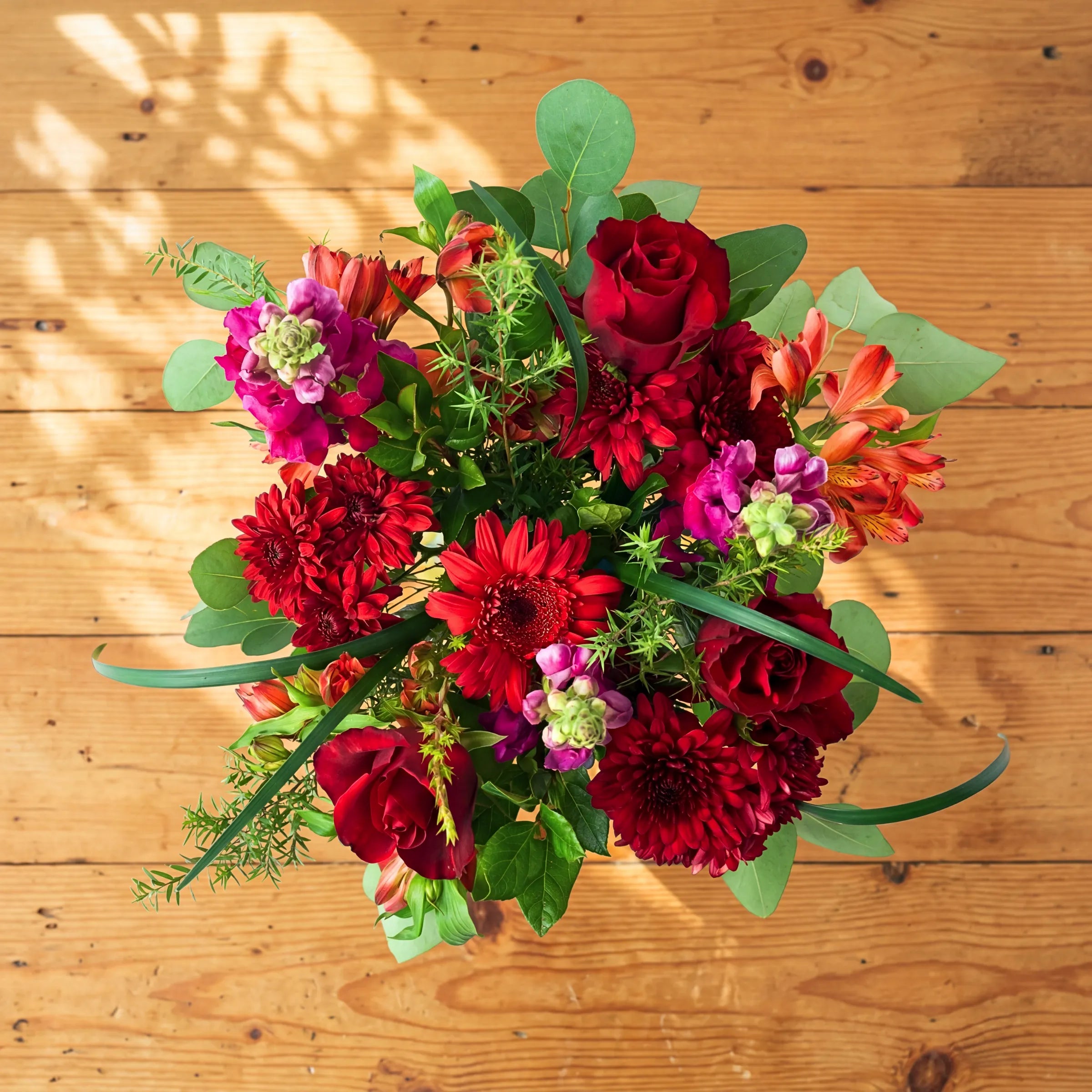 Overhead of the Charming red flower arrangement, red roses, chrysanthemums, orange alstroemeria and eucalyptus in a glass jar