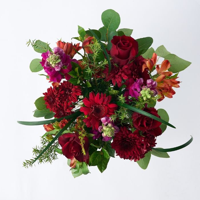 Top-down view of a vibrant flower arrangement featuring red roses, gerbera daisies, and mixed greenery.