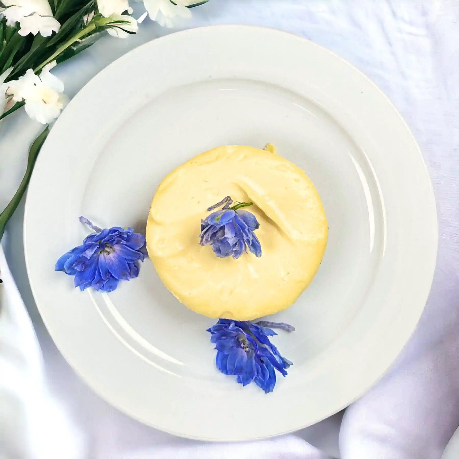 Delicious cheesecake garnished with blue flowers, elegantly placed on a white plate with floral accents. Fabulous Flowers and Gifts.