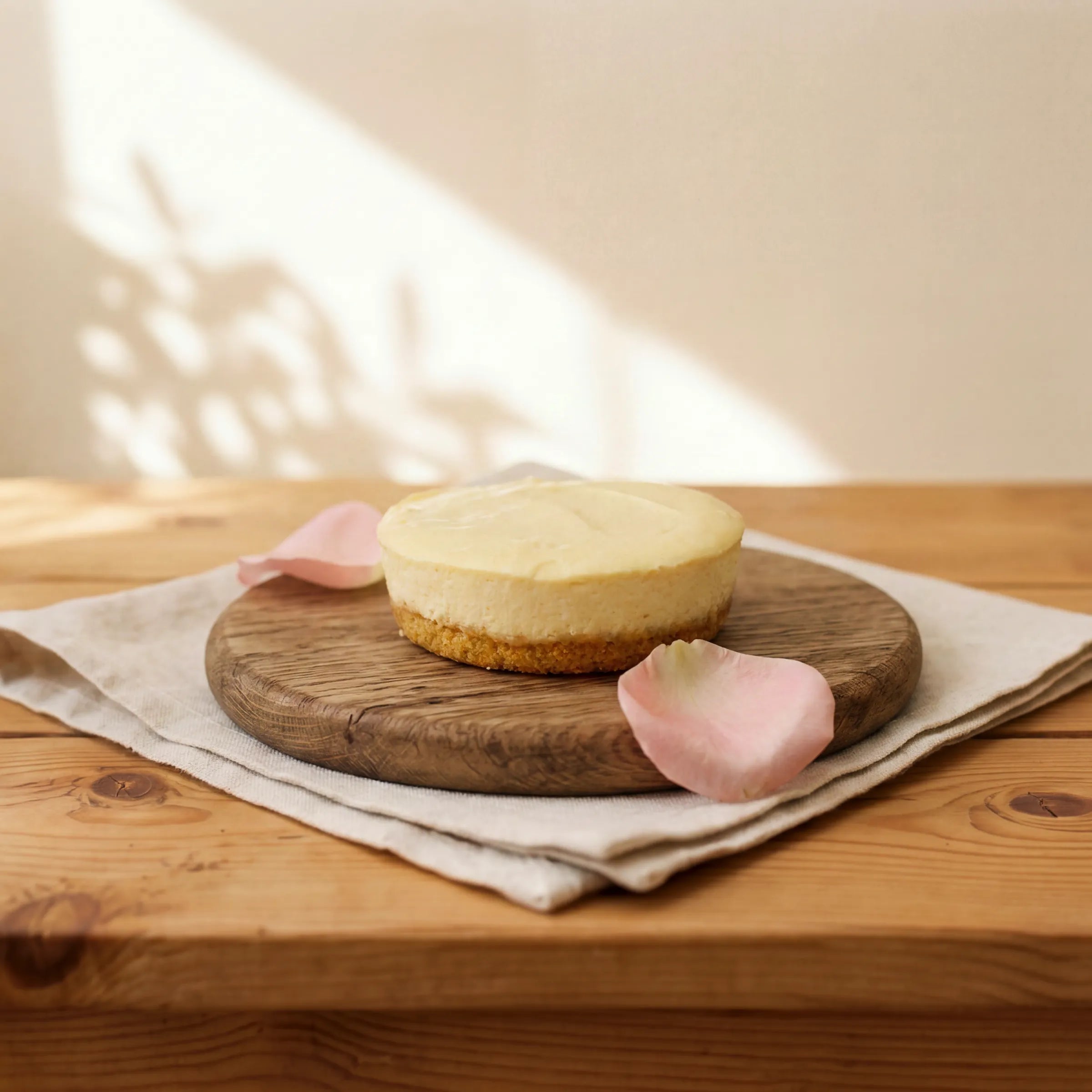 Lemon Cheesecake on oak board with pink rose petals and linen, by Fabulous Flowers Cape Town since 1999