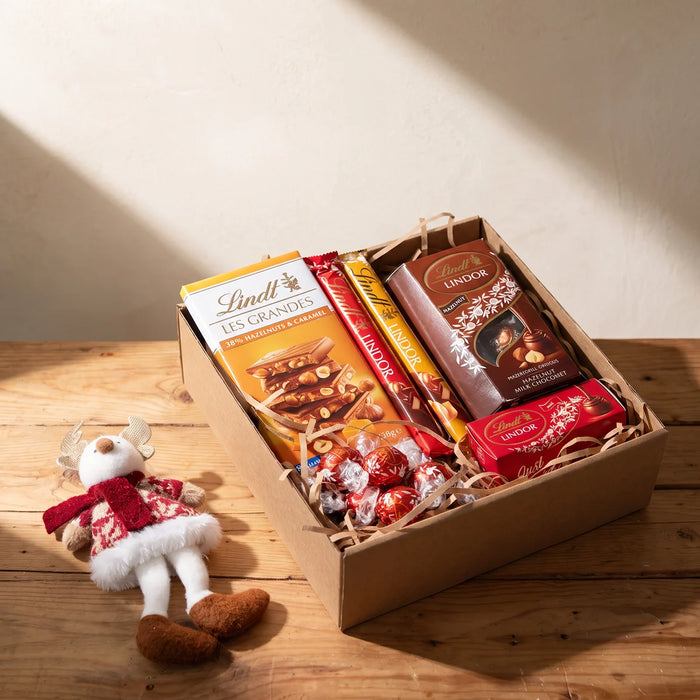 Open kraft gift box of Lindt chocolates with a plush reindeer ornament beside it on a pine table, Fabulous Flowers South Africa