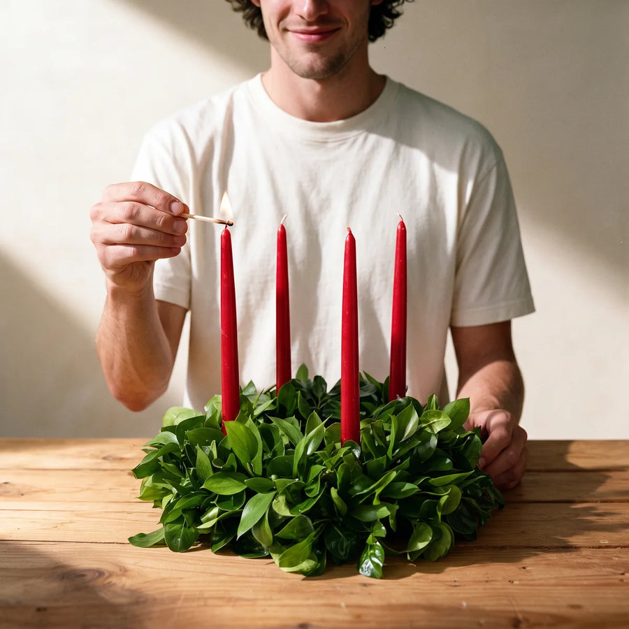 Man in a white t-shirt lighting a red candle on a fresh green table wreath with a match, Fabulous Flowers South Africa