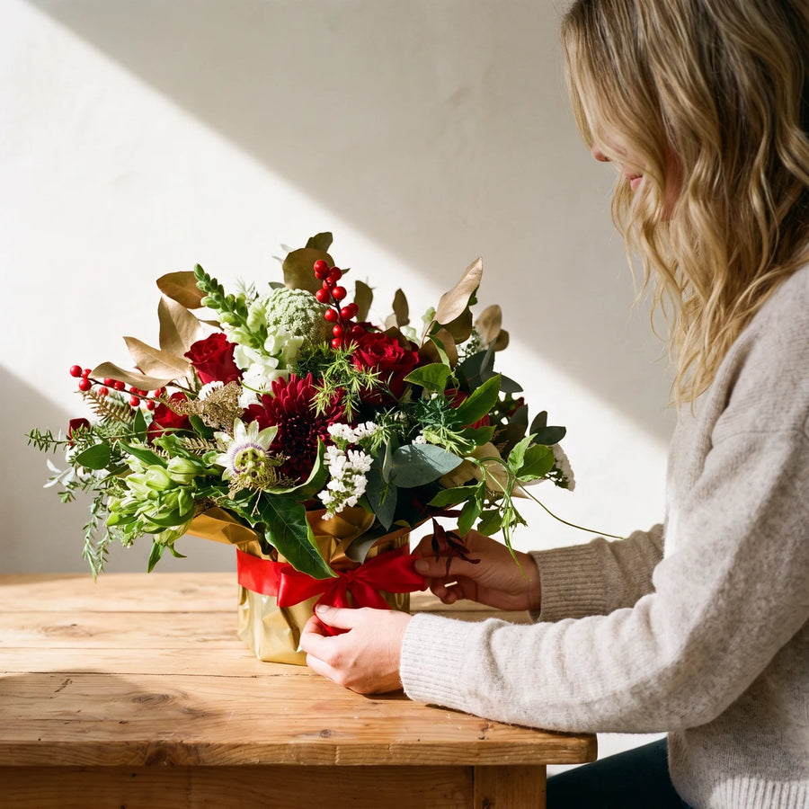 Woman in a knit jumper tying the red ribbon on a gold-wrapped Christmas flower arrangement, Fabulous Flowers South Africa
