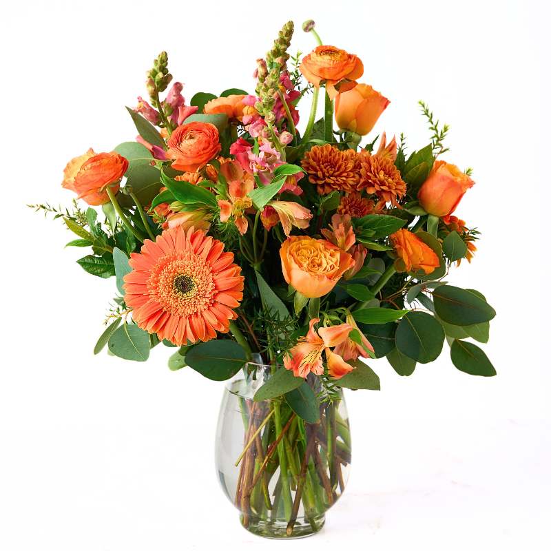 Citrus Couture Flower Arrangement in a clear glass vase with orange roses, gerberas, lilies and lush greenery