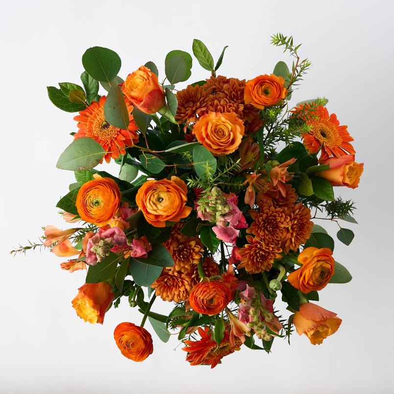 Top-down view of the Citrus Couture Flower Arrangement, showcasing bright orange gerberas, roses, snapdragons, and fresh greenery.