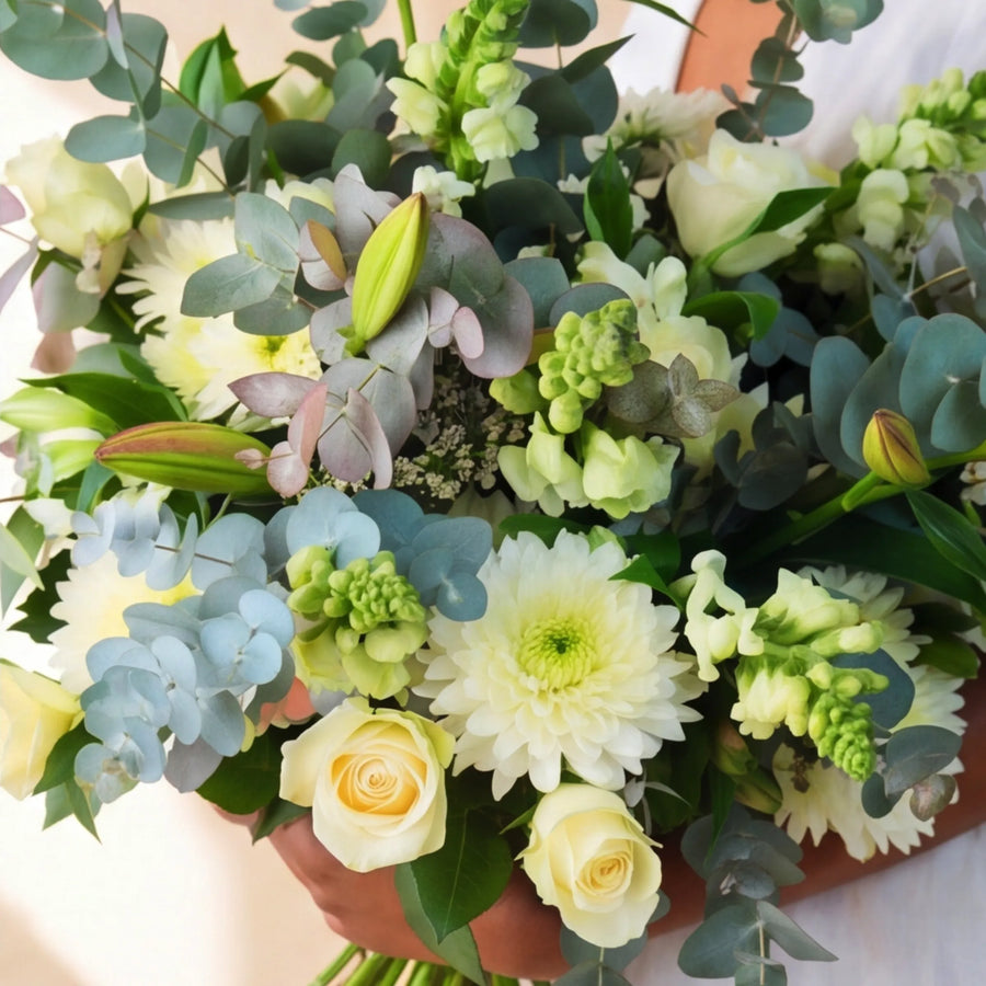 Top view of the Classic White Bouquet with cream roses, white chrysanthemums, blue hydrangea, green bells of Ireland and silver dollar eucalyptus
