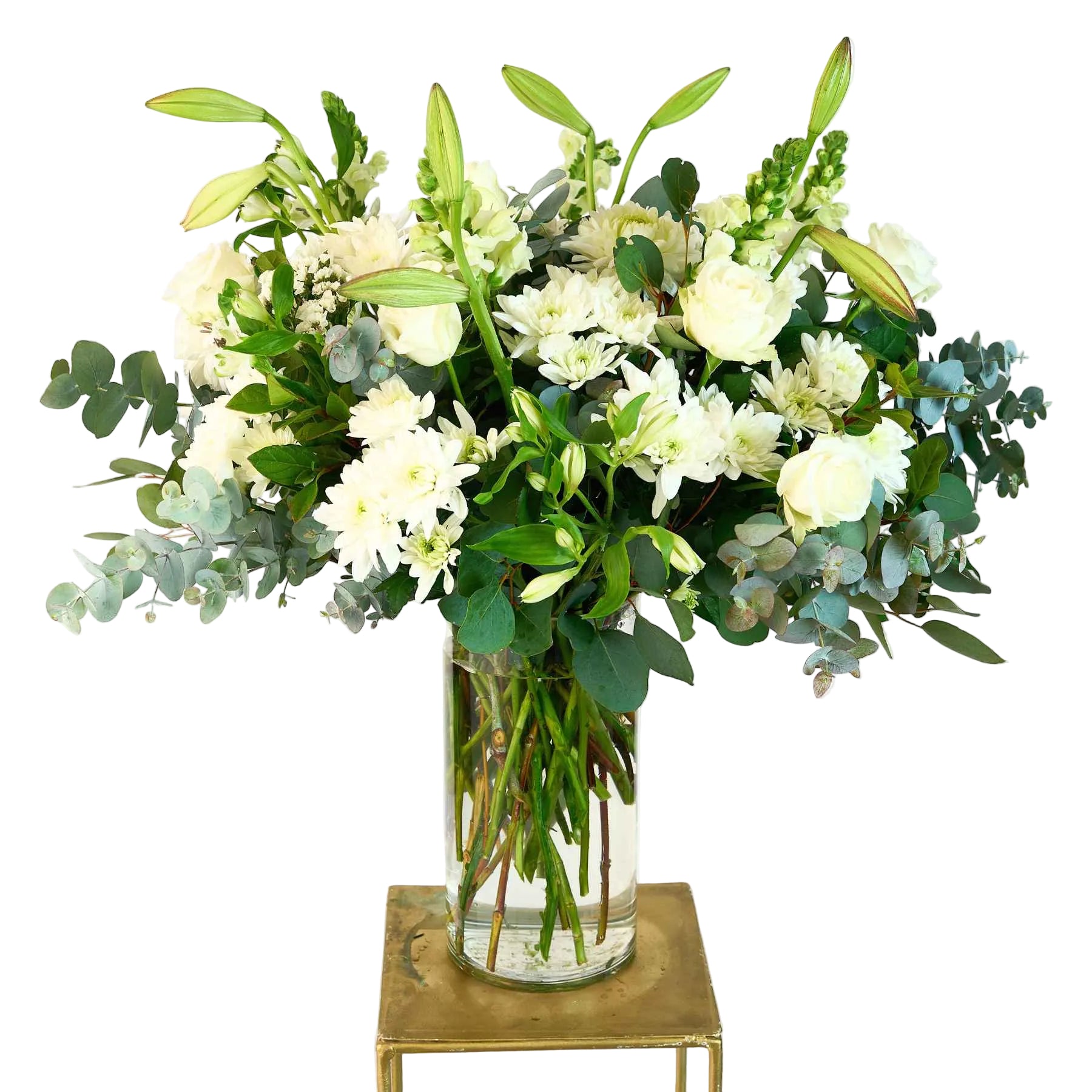 Elegant white flower arrangement in a glass vase, featuring roses, lilies, and lush green foliage, displayed on a minimalistic stand.