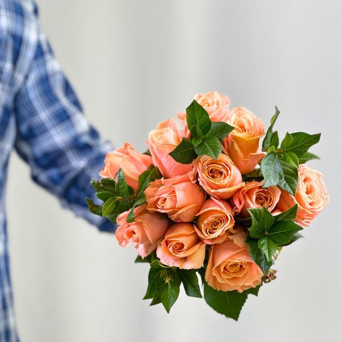 Coral Charm Rose Bouquet – vibrant coral roses with greenery, held in both hands, wrapped and ready to delight