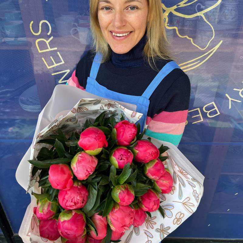 Top shot of smiling florist holding fresh bouquet of 20 peonies wrapped beautifully.