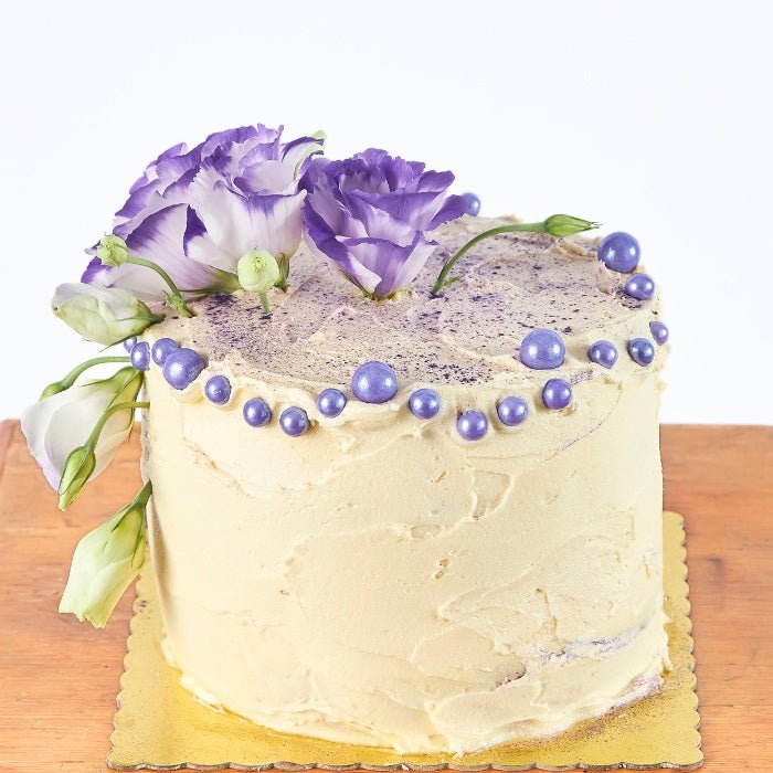 Creamy Violet Dream Cake - Fabulous Flowers & Gifts close-up of floral cake with purple pearl decorations and fresh blooms.