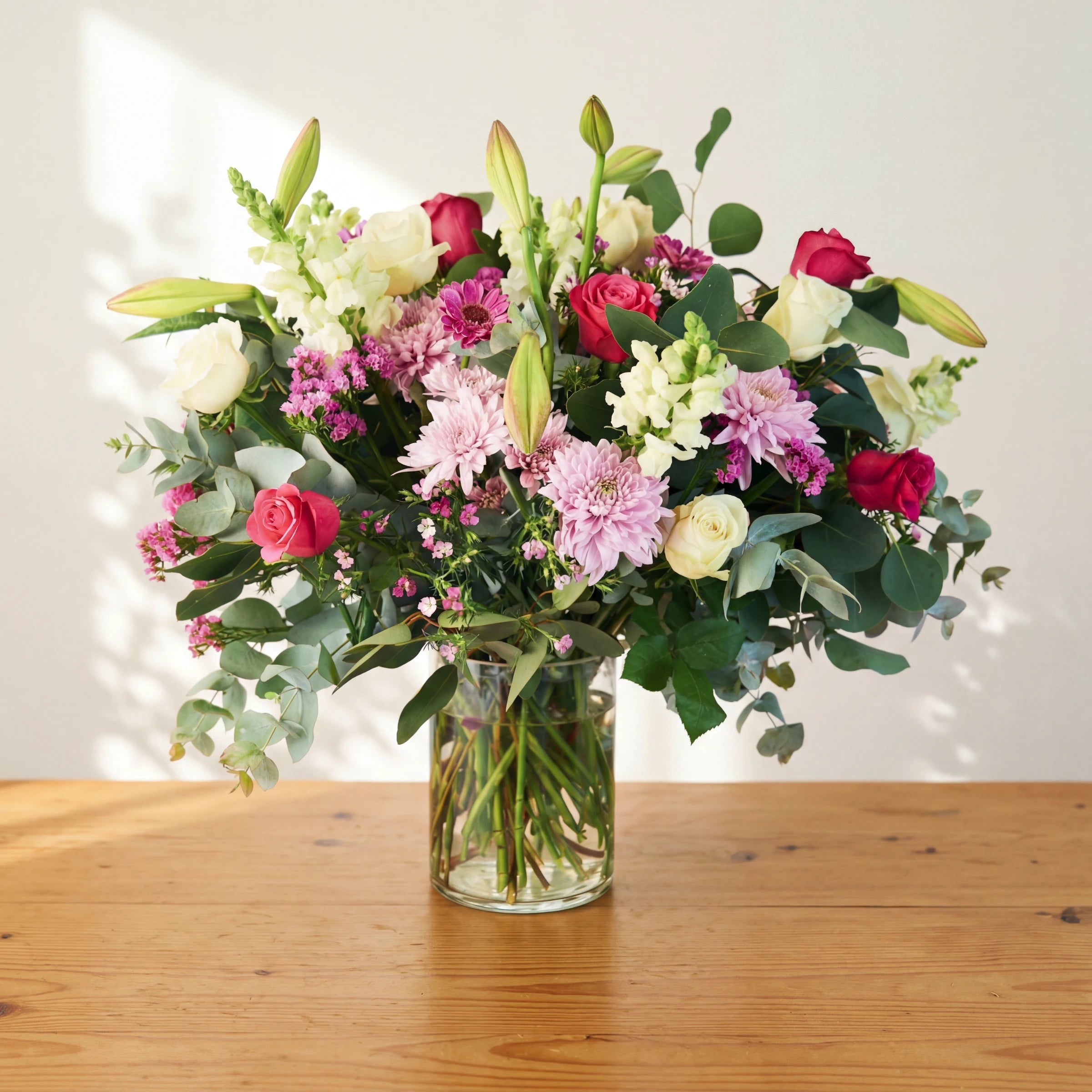 Pink and white flowers in a glass vase, white and cerise roses, lilac blooms, snapdragons and eucalyptus.
